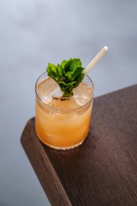 A refreshing mint-infused cocktail with ice cubes and a straw on a wooden table corner.