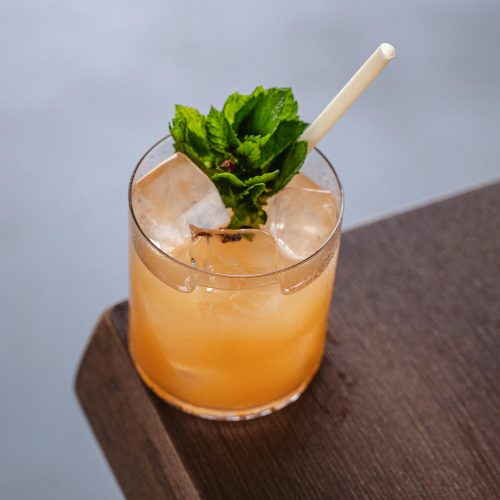 A refreshing mint-infused cocktail with ice cubes and a straw on a wooden table corner.